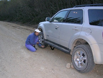 Evelyn Hamilton changing a flat tire on a remote gravel access road